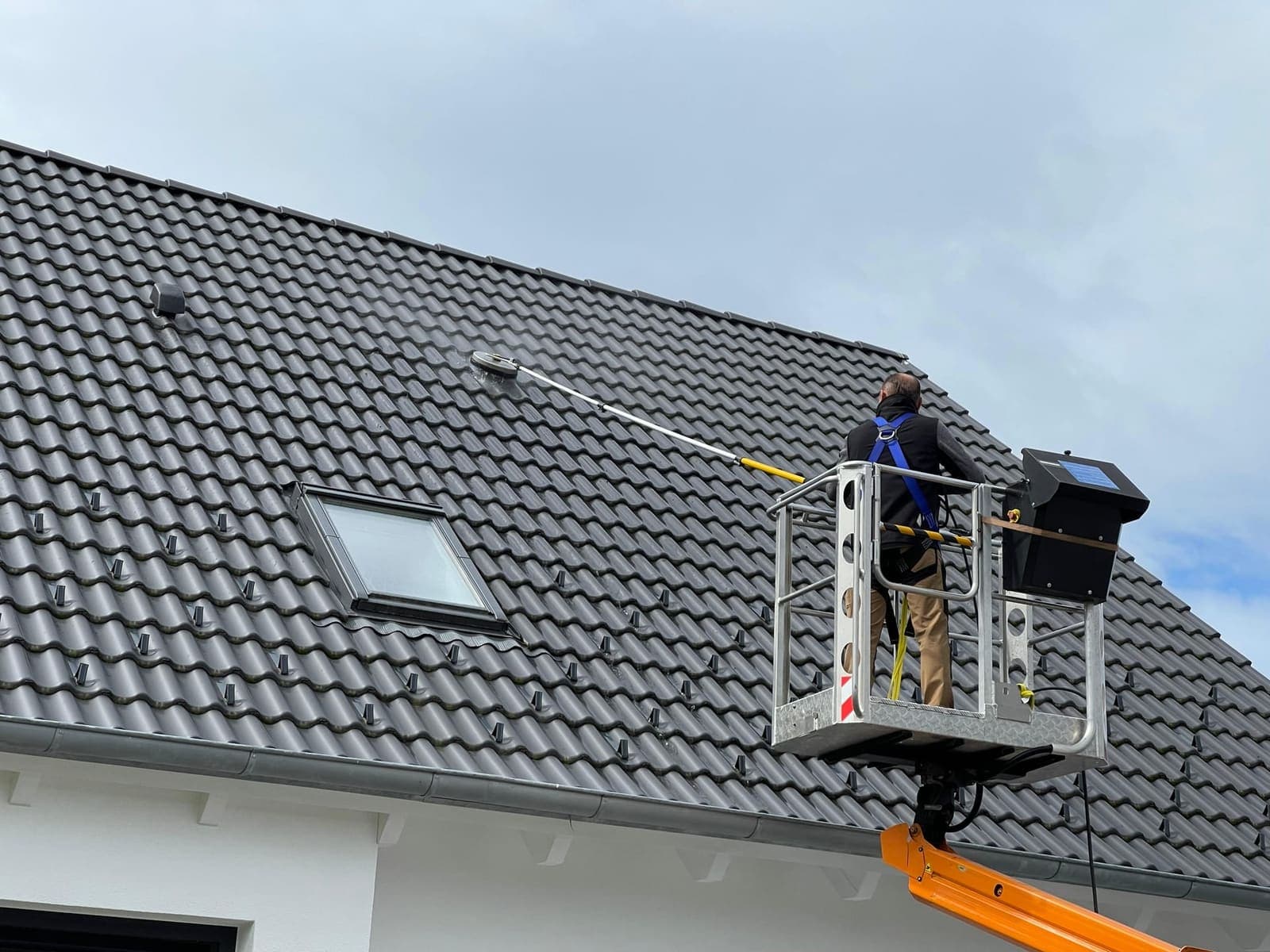 Mitarbeiter in Hubwagen reinigt Ziegeldach mit Flächenreiniger
