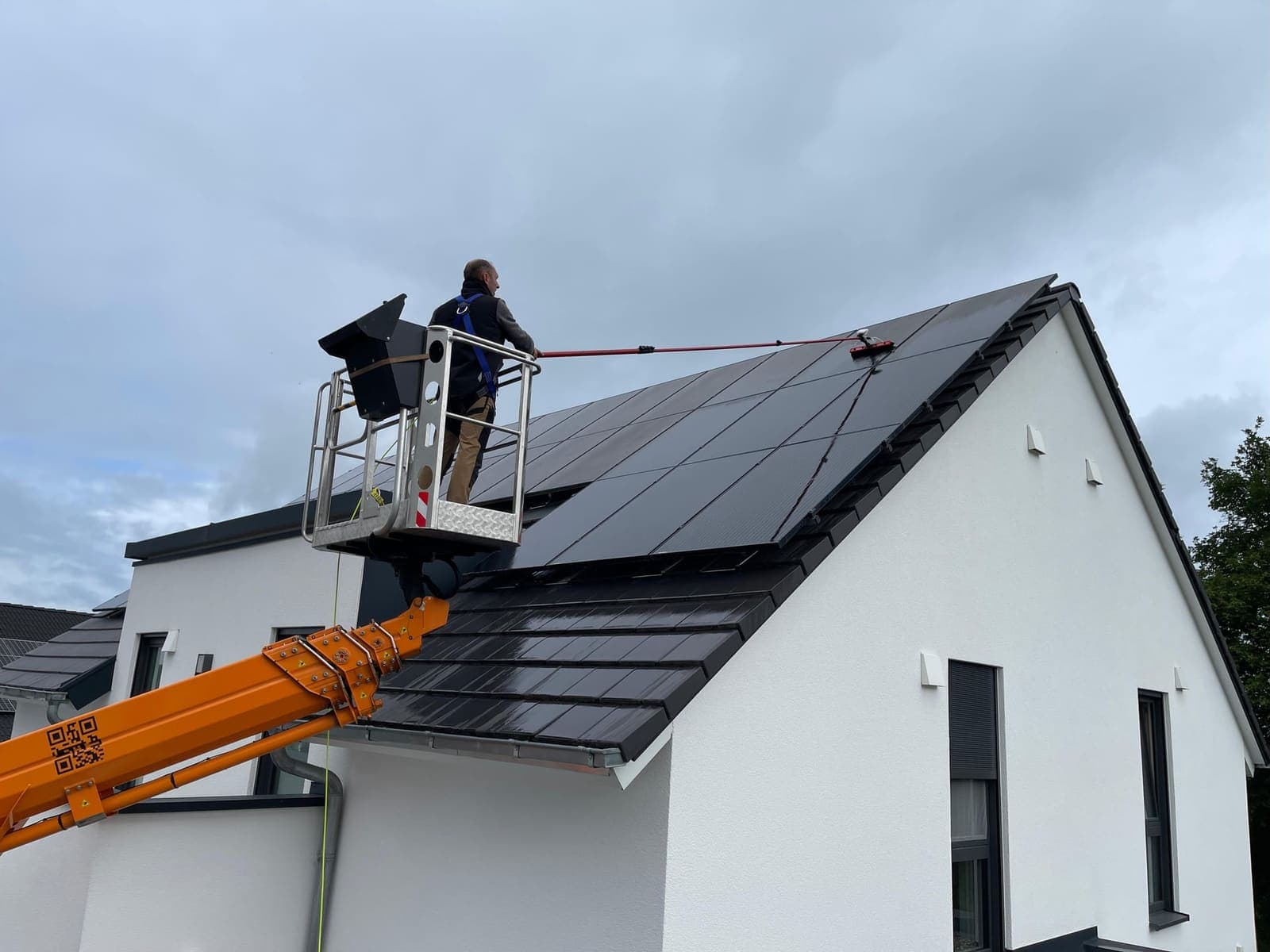 Mitarbeiter in Hebebühne reinigt Photovoltaik-Anlage auf Einfamilienhaus