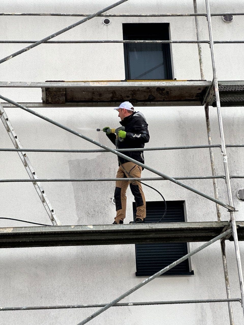Tissen-Mitarbeiter reinigt Hausfassade auf dem Gerüst mit Heißwasser-Hochdruck