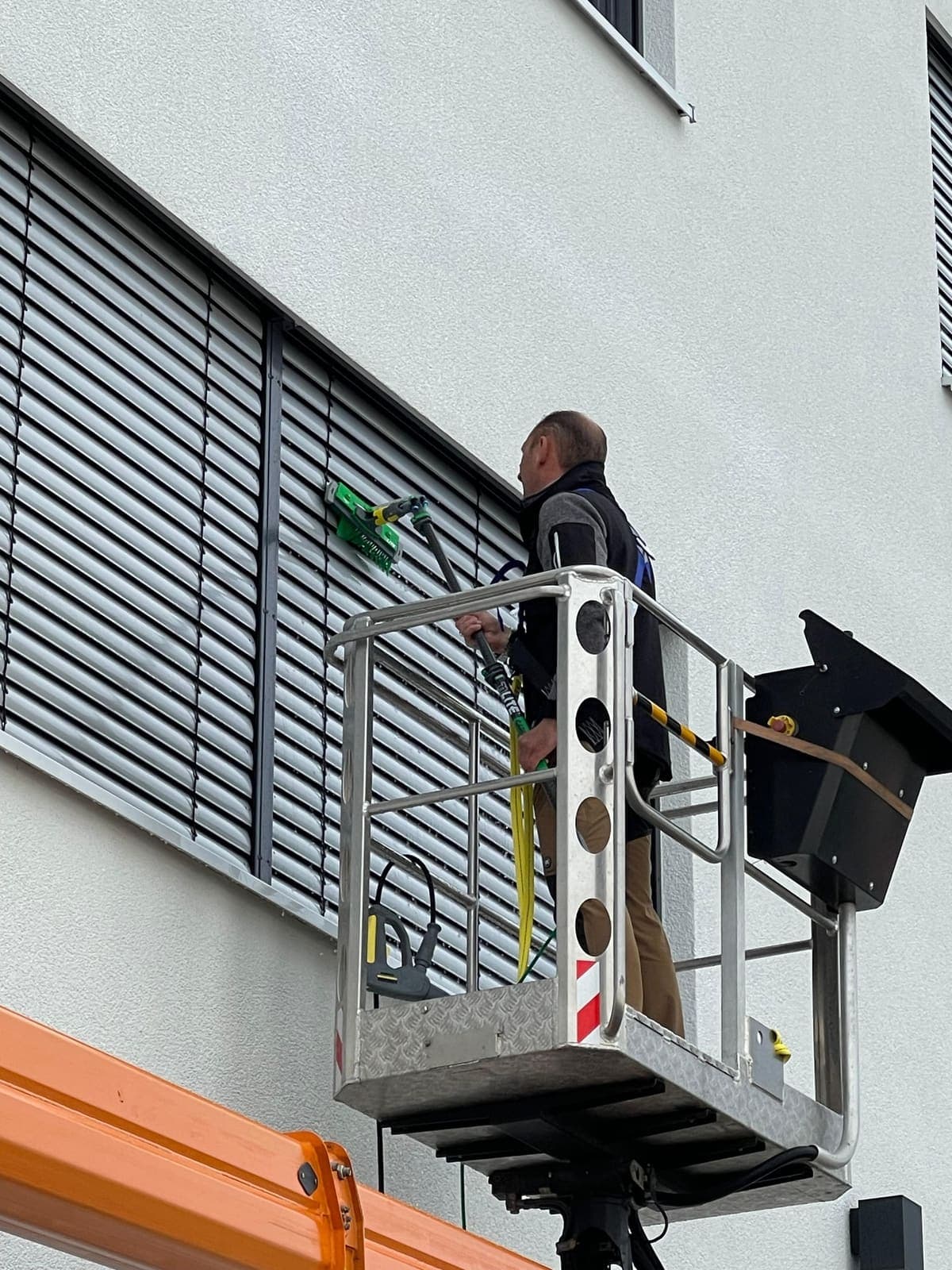 Mitarbeiter reinigt Außenjalousien am Gewerbegebäude aus der orangenen Hebebühne