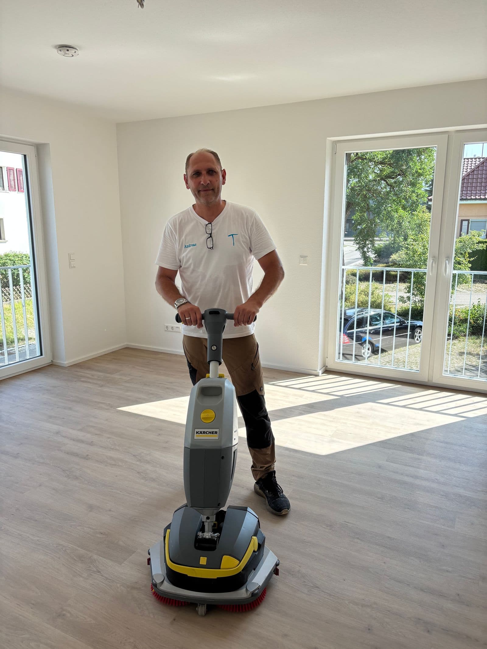Tissen-Mitarbeiter mit Kärcher-Scheuersaugmaschine in einem leeren, frisch gereinigten Wohnzimmer eines Neubaus