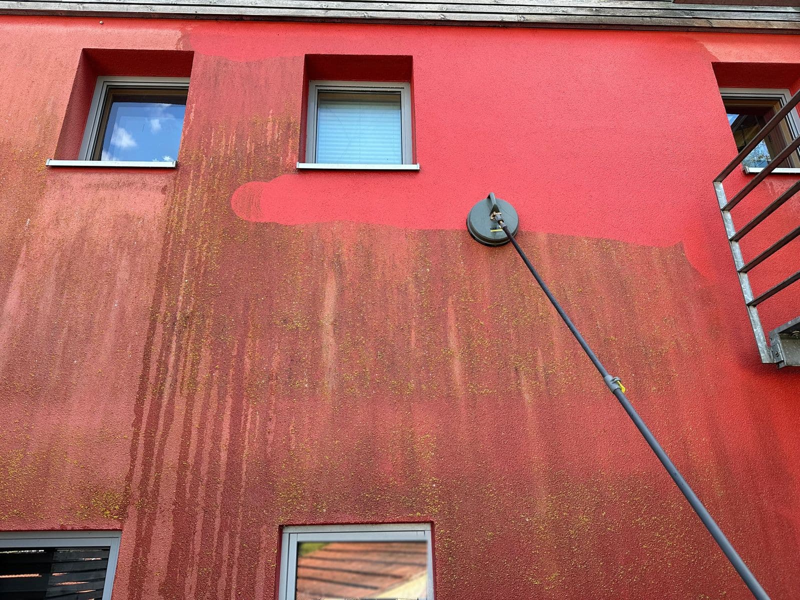 Rote Putzfassade während der Reinigung mit Rotationsteller – deutlicher Kontrast zwischen gereinigter und noch verschmutzter Fläche